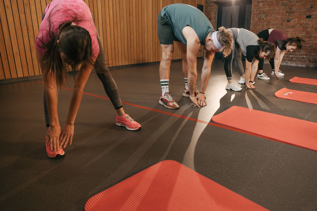 class-03 A diverse group of adults stretching on mats during a gym workout session.
